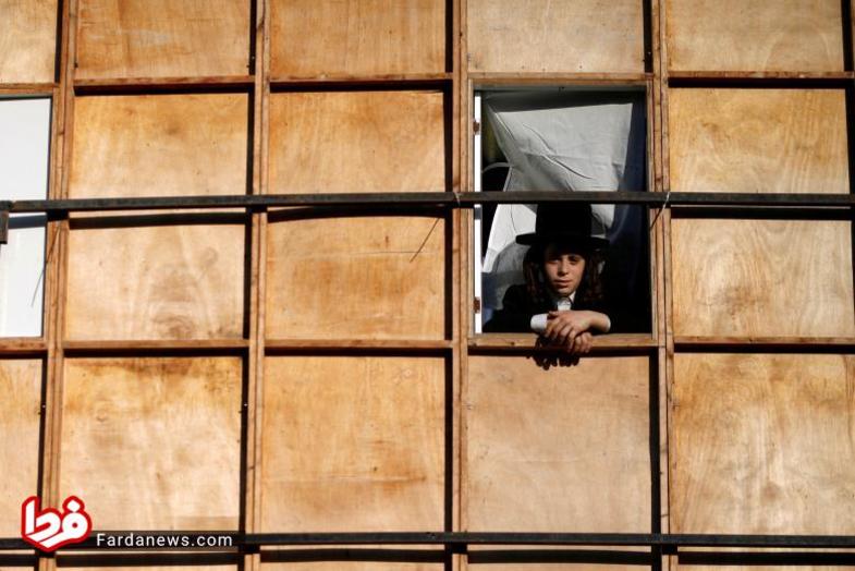 مرد جوان یهودی سرخود را از پنجره یکی از غرفه های که در مراسم برپا شده بیرون آورده است.